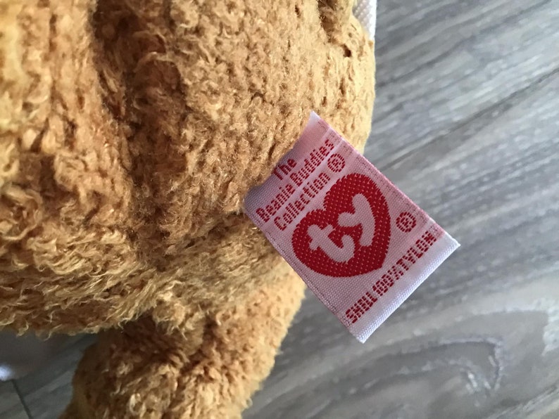 May include: A brown plush toy with a pink Ty tag that reads "The Beanie Babies Collection &copy; Ty Inc.  Small Only/Petite"