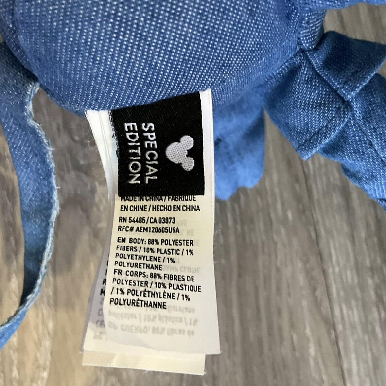 K&ouml;nnte beinhalten: Nahaufnahme eines blauen Pl&uuml;schtiers mit einem Etikett mit der Aufschrift "SPECIAL EDITION" und dem Mickey Mouse-Logo. Das Etikett listet auch die Materialien und das Herkunftsland auf.