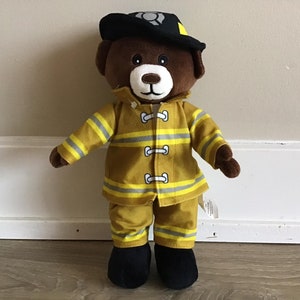 May include: A brown teddy bear wearing a yellow and black firefighter uniform with a black hat. The bear has a black nose and black eyes.