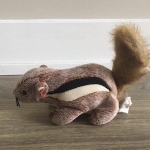 May include: A brown and white stuffed squirrel with a long, bushy tail. The squirrel has a black stripe across its back and a white stripe on its belly.