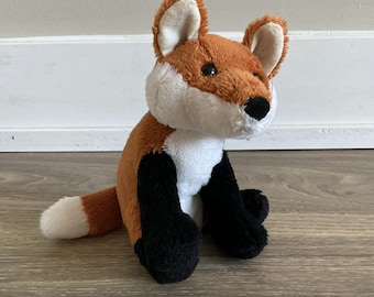 May include: A plush fox toy with orange fur, white belly, and black legs and feet. The fox is sitting with its tail curled behind it.