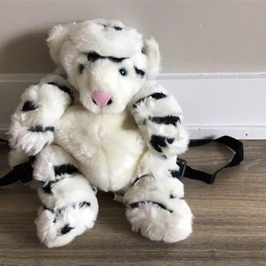 Op de afbeelding: Witte pluche tijgerrugzak met zwarte strepen. De rugzak heeft een verstelbare zwarte band.