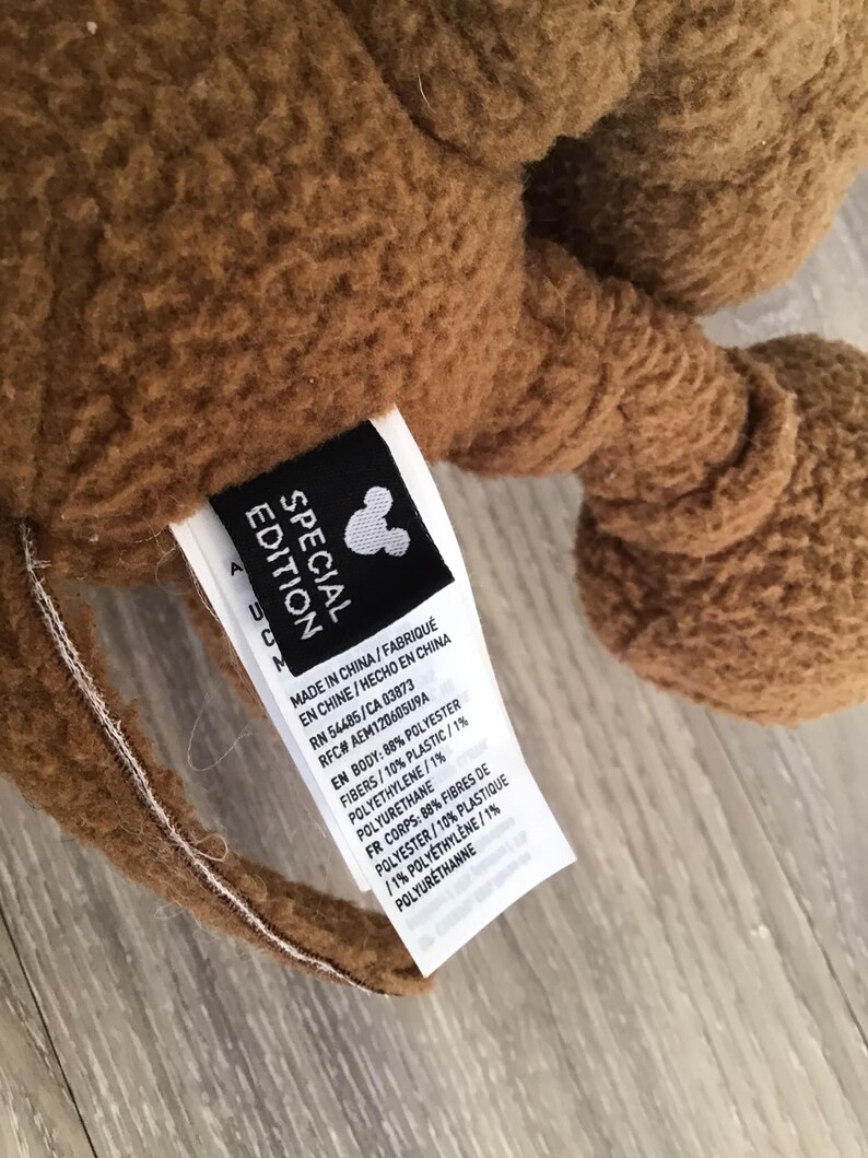 Puede incluir: Peluche marr&oacute;n con una etiqueta que dice "Edici&oacute;n especial" e incluye detalles sobre los materiales utilizados en su construcci&oacute;n. La etiqueta tambi&eacute;n incluye el logotipo de Disney y la siguiente informaci&oacute;n: Hecho en China/Fabrique en Chine/Hecho en China RN 54485/CA 03873 RFC# AEM12060509A EN Body: 88% Polyester Fibers/10% Plastic/1% Polyethylene/1% Polyurethane FR Corps: 88% Fibres de Polyester/10% Plastique /1% Polyethylene/1% Polyurethane