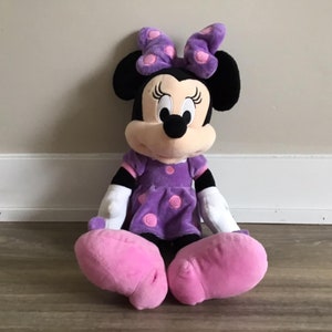 May include: A plush purple and pink Minnie Mouse toy with a purple polka dot dress and pink shoes.