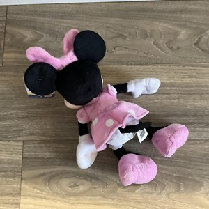 May include: A pink and black plush toy of Minnie Mouse. She is wearing a pink dress with white polka dots and has a pink bow on her head.