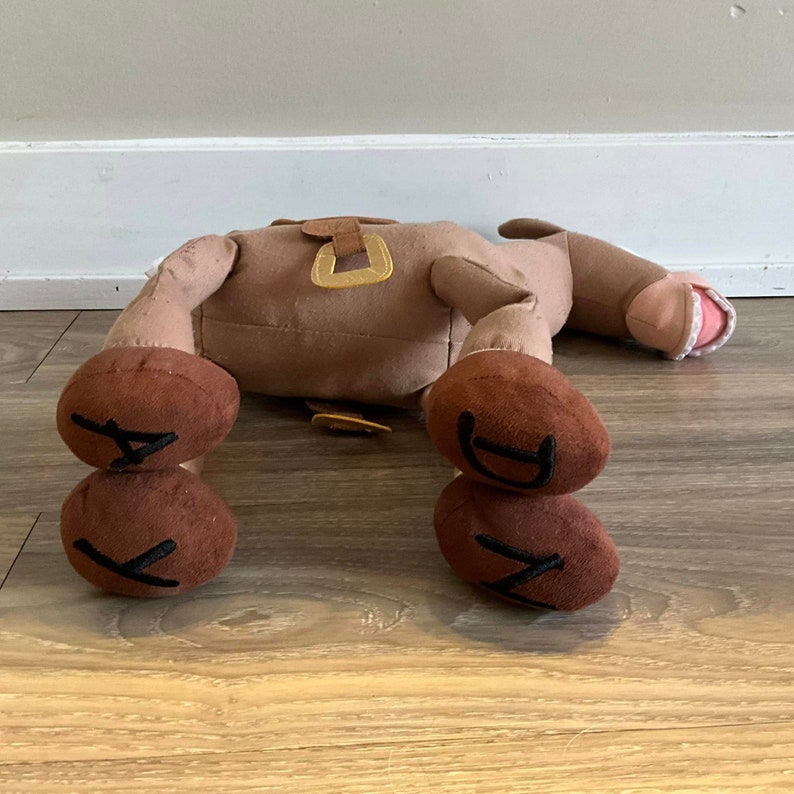Puede incluir: Un caballo de peluche marr&oacute;n con una silla de montar y estribos. El caballo est&aacute; tumbado de espaldas con las patas en el aire. Las pezu&ntilde;as del caballo son marrones y tienen las letras "KD" bordadas.