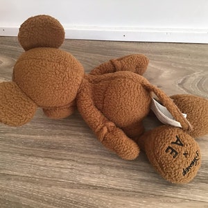 Puede incluir: Un juguete de peluche marr&oacute;n con forma de Mickey Mouse. El juguete est&aacute; tumbado de lado con la cabeza apoyada en el suelo. El juguete tiene el texto "A Bathing Ape x Disney" en su pie.