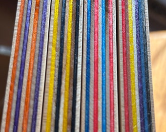 May include: Close-up of a stack of wooden boards with alternating layers of orange, purple, yellow, black, brown, blue, red, and white paint.