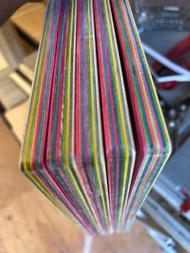 May include: Close-up of a stack of colorful, layered wood pieces. The edges reveal a vibrant array of colors including pink, yellow, green, and blue. The wood appears to be for a craft project or woodworking. The pieces are held together.