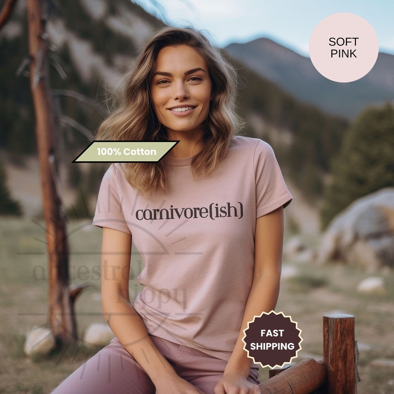 May include: A soft pink, 100% cotton t-shirt with the text "carnivore(ish)" printed on the front. The shirt is being worn by a person outdoors.