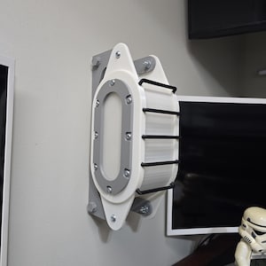 May include: A white and grey wall-mounted object with a rectangular window and black bars. The object is attached to the wall with bolts and has a futuristic design. It is likely a decorative or functional piece.
