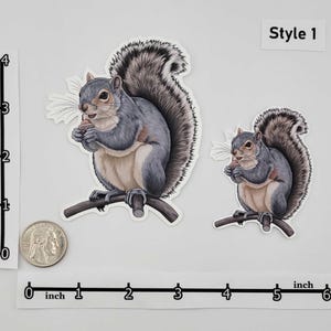 May include: Two squirrel stickers, one large and one small, both perched on a branch and holding a nut. The squirrels have gray fur and fluffy tails. The text "Style 1" is in the upper right corner.