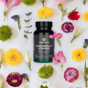 May include: A dark bottle of VitaRoots Inner Beauty Vitamins, set against a white backdrop with various flowers. The bottle, with a black lid and green base, displays the text "Inner Beauty Vitamins". The image features pink, yellow, and purple flowers.