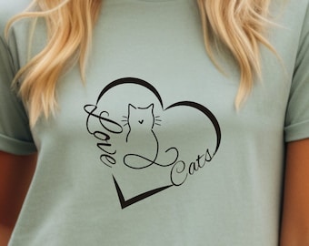 Può includere: Una maglietta verde chiaro con una grafica nera a forma di cuore con le parole "Love Cats" e un gatto seduto all'interno del cuore.
