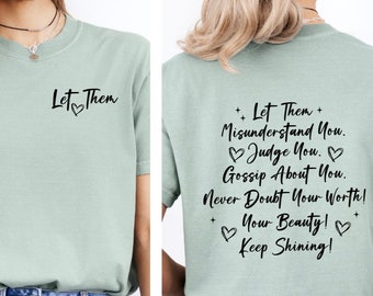 May include: A pale green t-shirt with the words "Let Them" and a heart on the front. The back of the shirt has the text "Let Them Misunderstand You. Judge You. Gossip About You. Never Doubt Your Worth! Your Beauty! Keep Shining!"