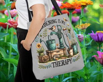 May include: A gray tote bag with a floral design and the text "Gardening is my therapy". The bag features a hand-drawn illustration of a well pump, watering cans, and gardening tools.