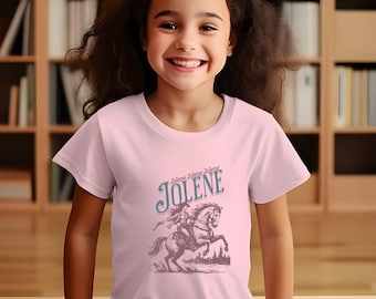 Op de afbeelding: Een roze T-shirt met een vintage-stijl illustratie van een vrouw die op een paard rijdt. De tekst "Jolene Jolene Jolene" is in blauw boven de afbeelding gedrukt.