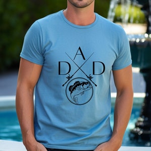 May include: A blue t-shirt with a black graphic design of two crossed fishing rods with a fish in a circle and the letters "DAD" and "A" in the center.