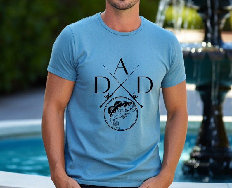 May include: A blue t-shirt with a black graphic design of two crossed fishing rods with a fish in a circle and the letters "DAD" and "A" in the center.