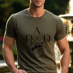 May include: A green t-shirt with a black graphic design of two fishing rods crossed with the letters "D A D" and a fish in the center.