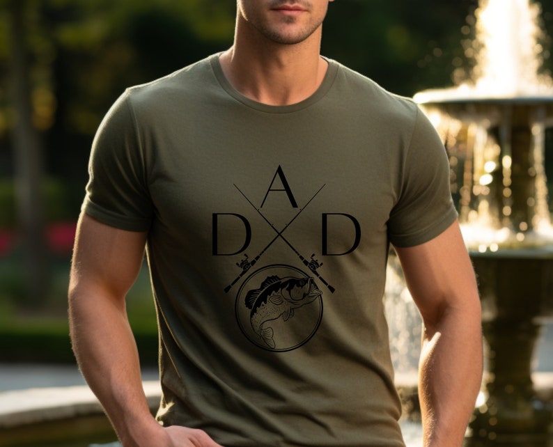 May include: A green t-shirt with a black graphic design of two fishing rods crossed with the letters "D A D" and a fish in the center.