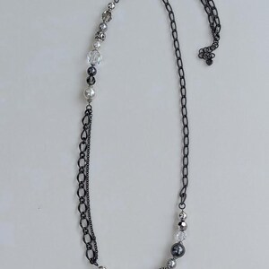 Puede incluir: Un collar largo con una cadena de metal de ca&ntilde;&oacute;n de fusil y una secci&oacute;n de cuentas. La secci&oacute;n de cuentas presenta una mezcla de perlas, cristales transparentes y cuentas grises. El collar se muestra sobre un fondo blanco.