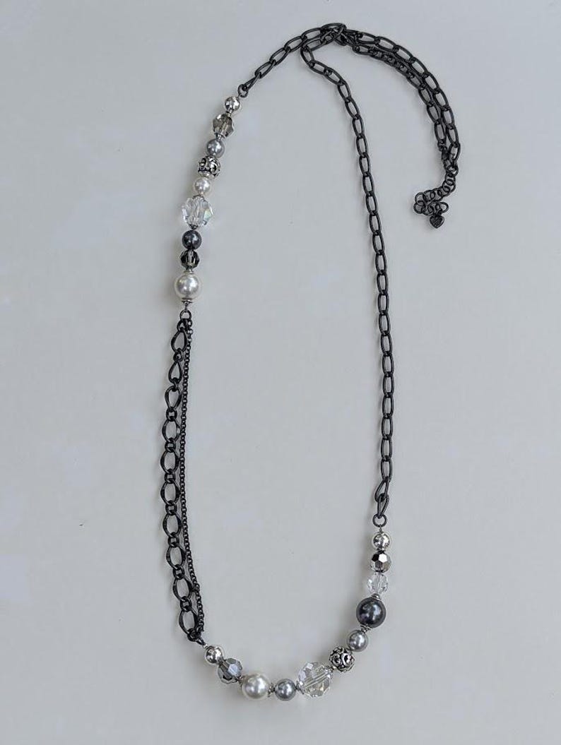 Puede incluir: Un collar largo con una cadena de metal de ca&ntilde;&oacute;n de fusil y una secci&oacute;n de cuentas. La secci&oacute;n de cuentas presenta una mezcla de perlas, cristales transparentes y cuentas grises. El collar se muestra sobre un fondo blanco.