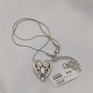 May include: Silver heart pendant necklace with a pearl-like centre and clear crystal accents. The heart design features swirling details and is suspended from a delicate chain. A tag with the text "LACRIMA JN2642 Brighton" is attached.