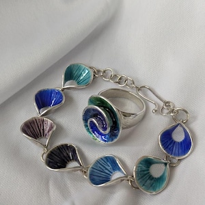 May include: A silver bracelet and ring set with blue, green, and purple enamel. The bracelet is made of a chain with teardrop-shaped links, each with a different color enamel. The ring is a swirl design with blue, green, and purple enamel.