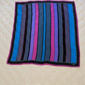 May include: A square silk scarf with a striped pattern in shades of blue, purple, pink, and black. The scarf has a thin black border and a pink border.