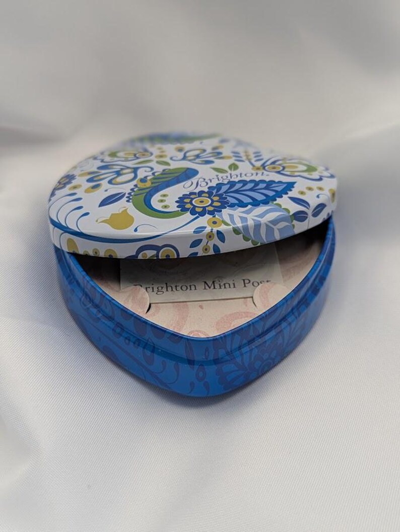 K&ouml;nnte beinhalten: Eine herzf&ouml;rmige Dose mit Klappdeckel, blau und wei&szlig; bemalt mit einem Blumen- und Paisley-Design. Der Deckel ist ge&ouml;ffnet und zeigt das Innere und den Text "Brighton Mini Pouch".