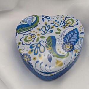 K&ouml;nnte beinhalten: Herzf&ouml;rmige dekorative Dose mit blauem, gr&uuml;nem und gelbem Blumenmuster auf wei&szlig;em Hintergrund. Die Dose hat einen blauen Rand und das Wort "Brighton" ist auf dem Deckel aufgedruckt.