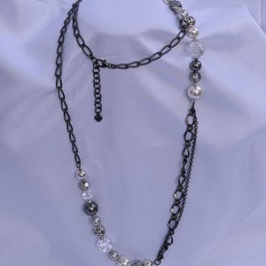 Puede incluir: Un collar largo con una cadena de metal de ca&ntilde;&oacute;n de fusil y varias cuentas. Las cuentas incluyen cuentas claras facetadas, plateadas y con forma de perla. El collar tiene un dise&ntilde;o en capas con una cadena y un hilo de cuentas.