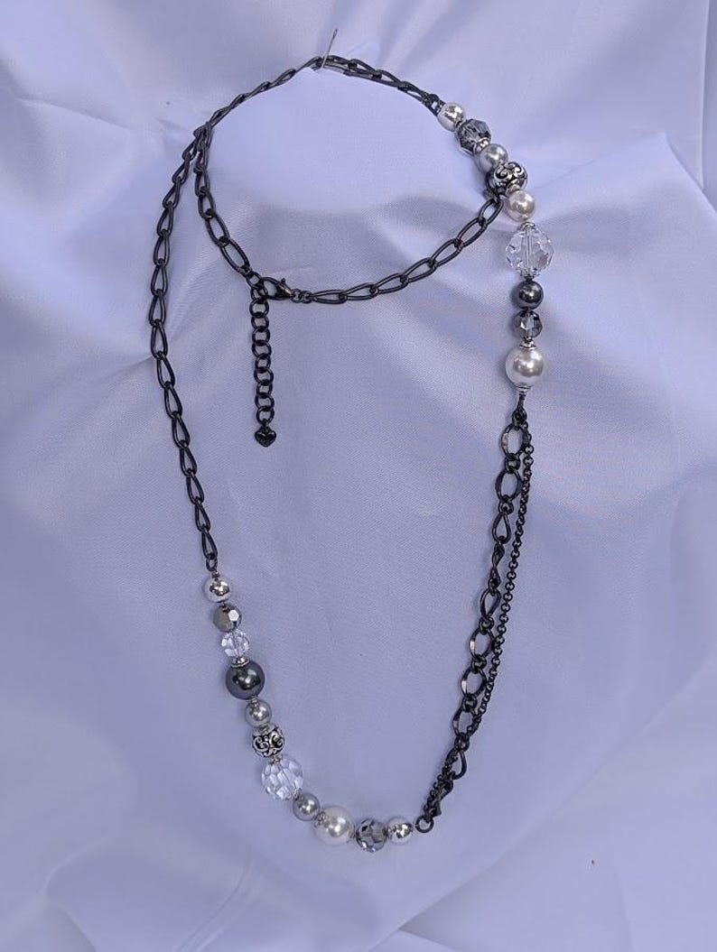 Puede incluir: Un collar largo con una cadena de metal de ca&ntilde;&oacute;n de fusil y varias cuentas. Las cuentas incluyen cuentas claras facetadas, plateadas y con forma de perla. El collar tiene un dise&ntilde;o en capas con una cadena y un hilo de cuentas.