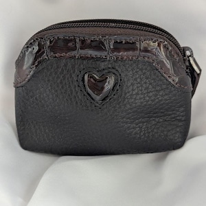 以下が含まれることがあります： ハート型のアクセントが付いた、小さな濃い茶色の小銭入れ。 質感のある革のボディと、光沢のあるクロコダイルエンボス加工のトップ部分が特徴です。 ジッパー開閉と小さなプルが付いています。