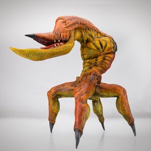 May include: A detailed, orange and yellow, sculpted figure of a creature with a long, thin neck, a beak-like mouth, and four clawed legs.