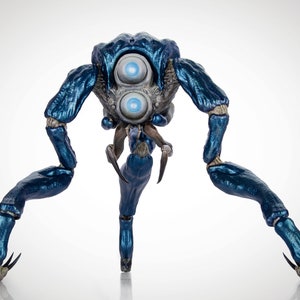 Puede incluir: Una criatura azul articulada de múltiples patas con dos ojos grandes y redondos. La criatura tiene un brillo metálico y garras afiladas.