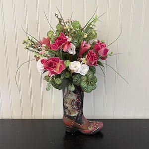 Arreglo floral en forma de bota con ciclamen y amapolas, y diseños únicos en la bota. Centro de mesa perfecto para cualquier ocasión.