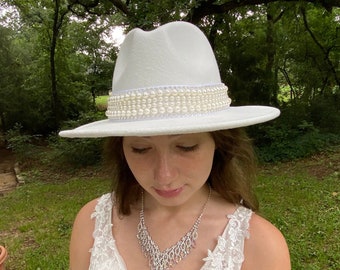 White bridal wedding fedora hat with hat band of rows of ivory pears. The back is accented with a white ribbon bow.