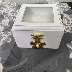 Ring bearer box. White with gold circle of hearts with pearl center. Clear top with white satin padded ring holder. Holds two rings.