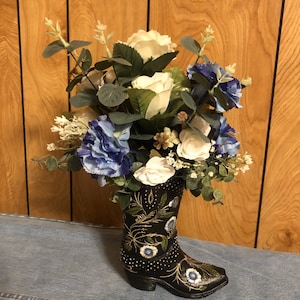 Flower arrangement in black resin boot with beautiful look of tooled leather, white flowers & gold vines, leaves. Large quantities available