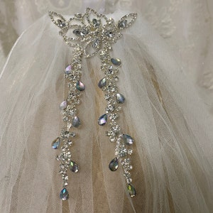 May include: A white bridal veil with a silver rhinestone floral design and dangling teardrop crystals.