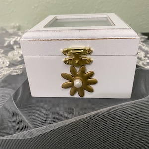 Ring bearer box. White with gold flower with pearl accent in center. Clear top with white satin padded ring holder. Holds two rings.