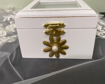 Ring bearer box. White with gold flower with pearl accent in center. Clear top with white satin padded ring holder. Holds two rings.