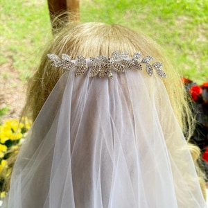 Peut inclure: Un voile en tulle blanc fixé sur un peigne à cheveux argenté orné d'un motif en forme de feuilles. Les feuilles métalliques sont incrustées de petits strass transparents et étincelants disposés de manière symétrique sur le haut du voile.