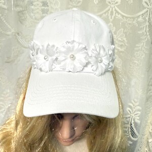 Witte bruid, bruidsmuts verfraaid met witte bloemen met parels in het midden en sluier op taillelengte bevestigd met Bride To Be on Veil