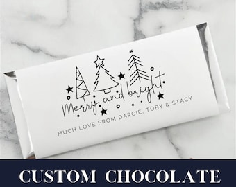 May include: A white chocolate bar wrapper with a black and white design of Christmas trees and stars. The text "Merry and bright." is written in a handwritten font. The text "Much love from Darcie, Toby & Stacy" is also included.
