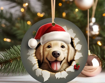 May include: A round Christmas ornament featuring a golden retriever puppy wearing a red Santa hat. The puppy is peeking through a torn piece of paper with a festive holly sprig.