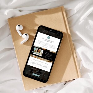 A smartphone displaying a webpage about training courses, placed on a tan notebook with white earphones beside it, resting on a soft white surface.