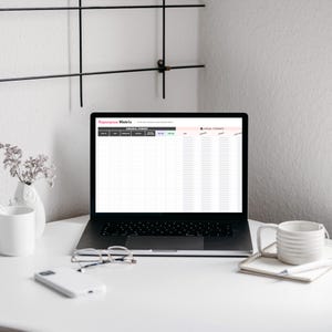 A laptop displaying a 'Repurpose Matrix' spreadsheet sits on a clean white desk with a coffee mug, glasses, and a notepad. Decorative elements include a small flower vase and a minimalist wall shelf.